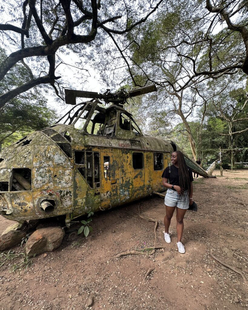 Woman Traveling The World. Woman Standing Next To An Old Helicopter In Accra, Ghana. Helicopter Found in Aburi Botanical Gardens. Woman Is The Weekend Traveler. Immersive Experiences in Accra, Ghana. Travel Africa.