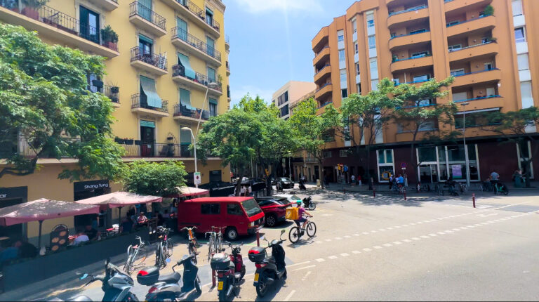 A random street in Barcelona with yellow and orange buildings. Also seen is a red bus and mopeds. Solo Trip to Barcelona.