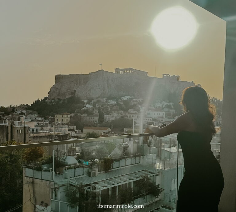 Woman on a balcony in Athens with a view of The Acropolis.